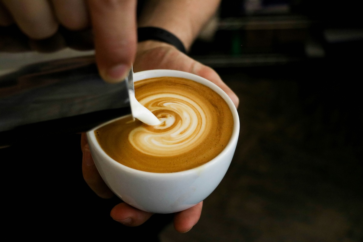 Barista hands creating spiral latte art in cappuccino with white cup
