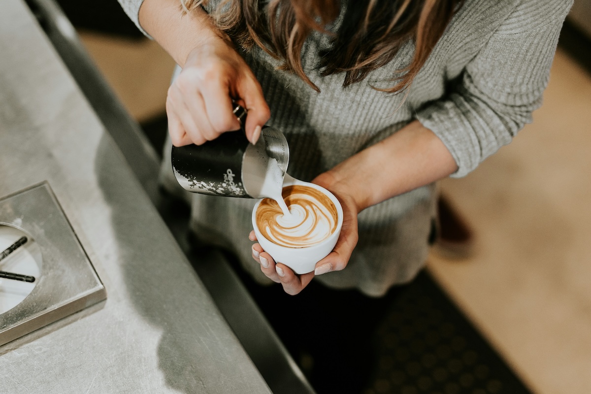 Barista pouring steamed milk creating latte art in white cup