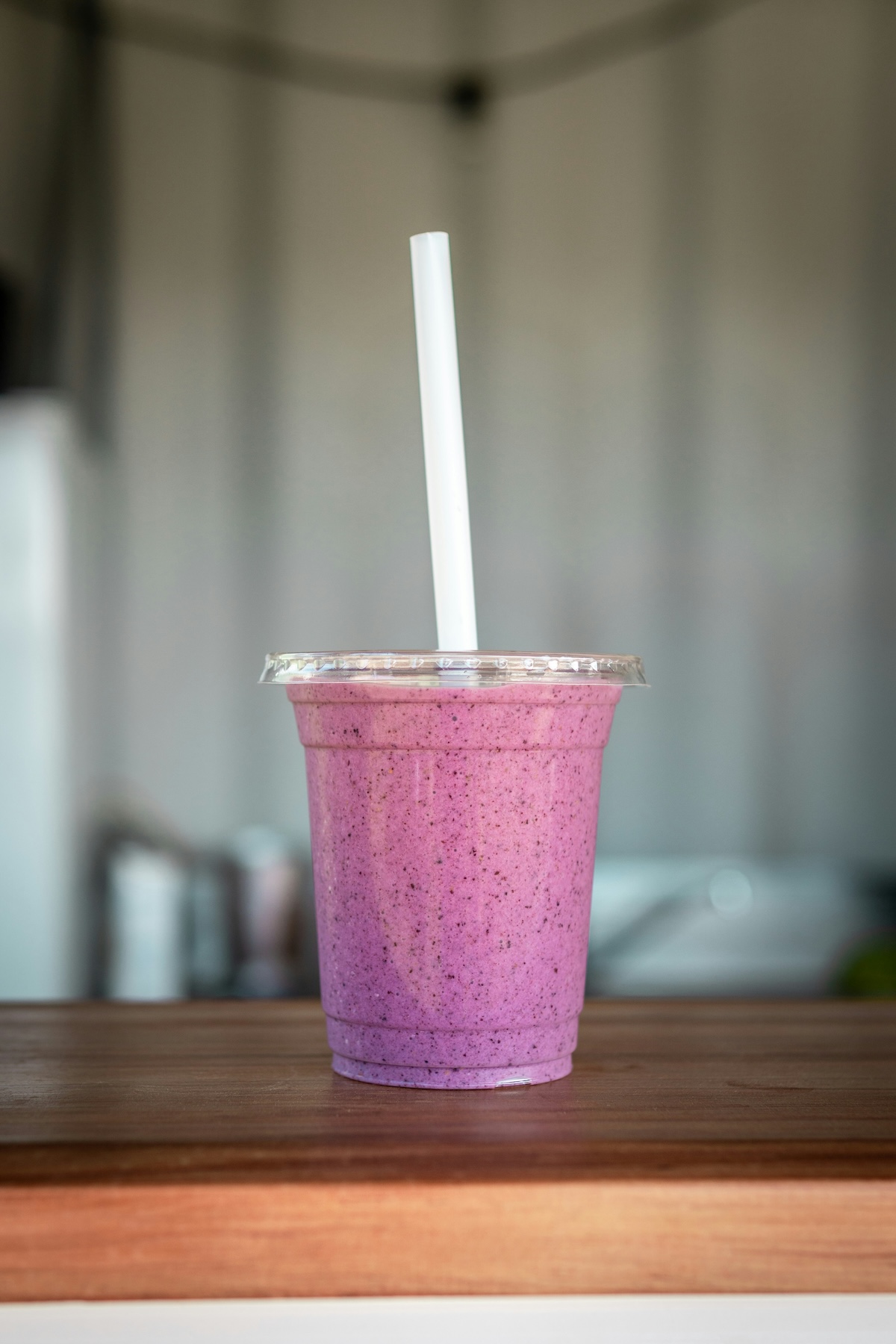 Purple berry smoothie in clear plastic cup with white straw on wooden table