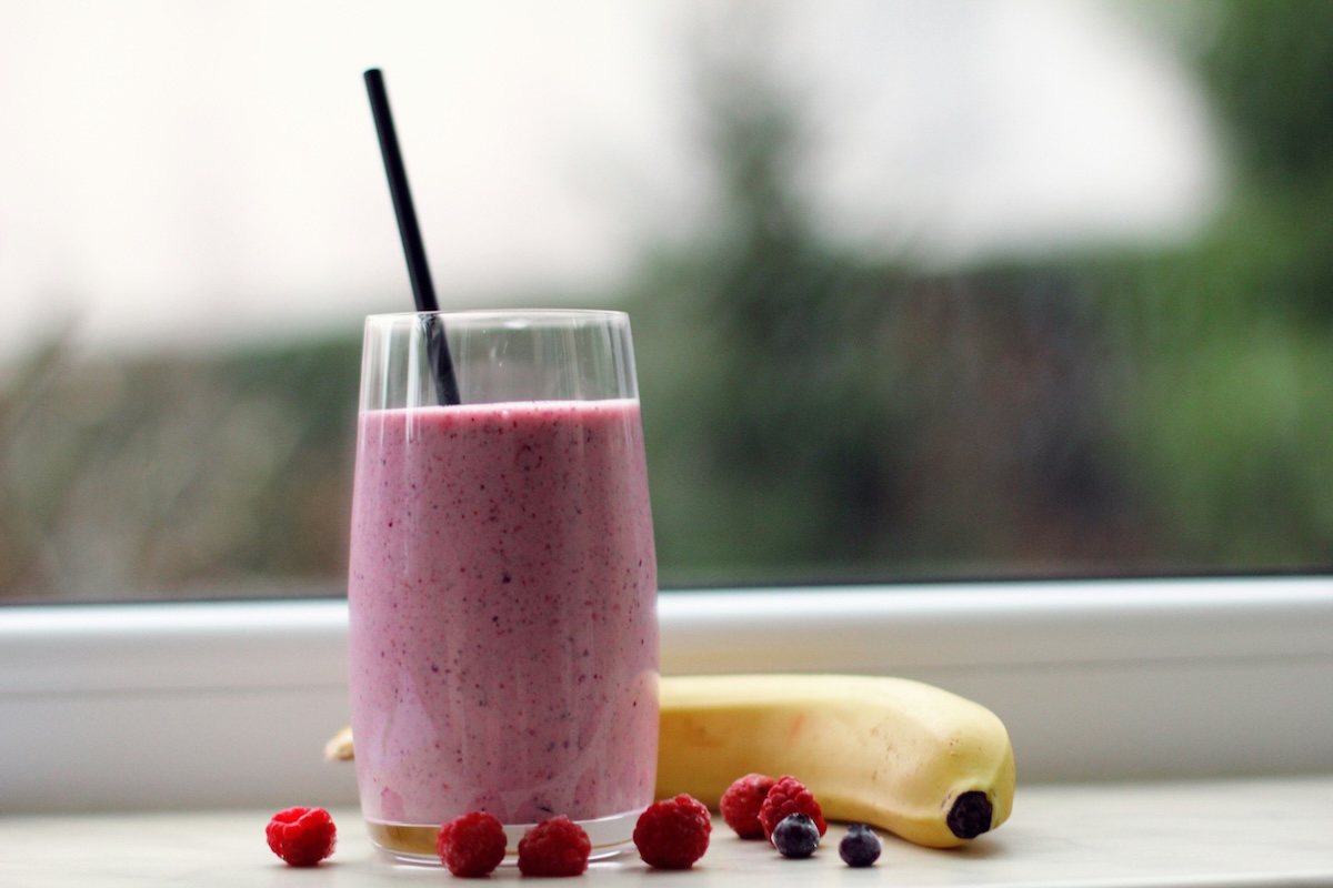Purple berry smoothie in glass with fresh raspberries, blueberries and banana on windowsill