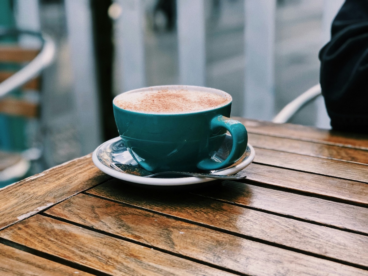 Chai latte in teal cup on outdoor cafe wooden table
