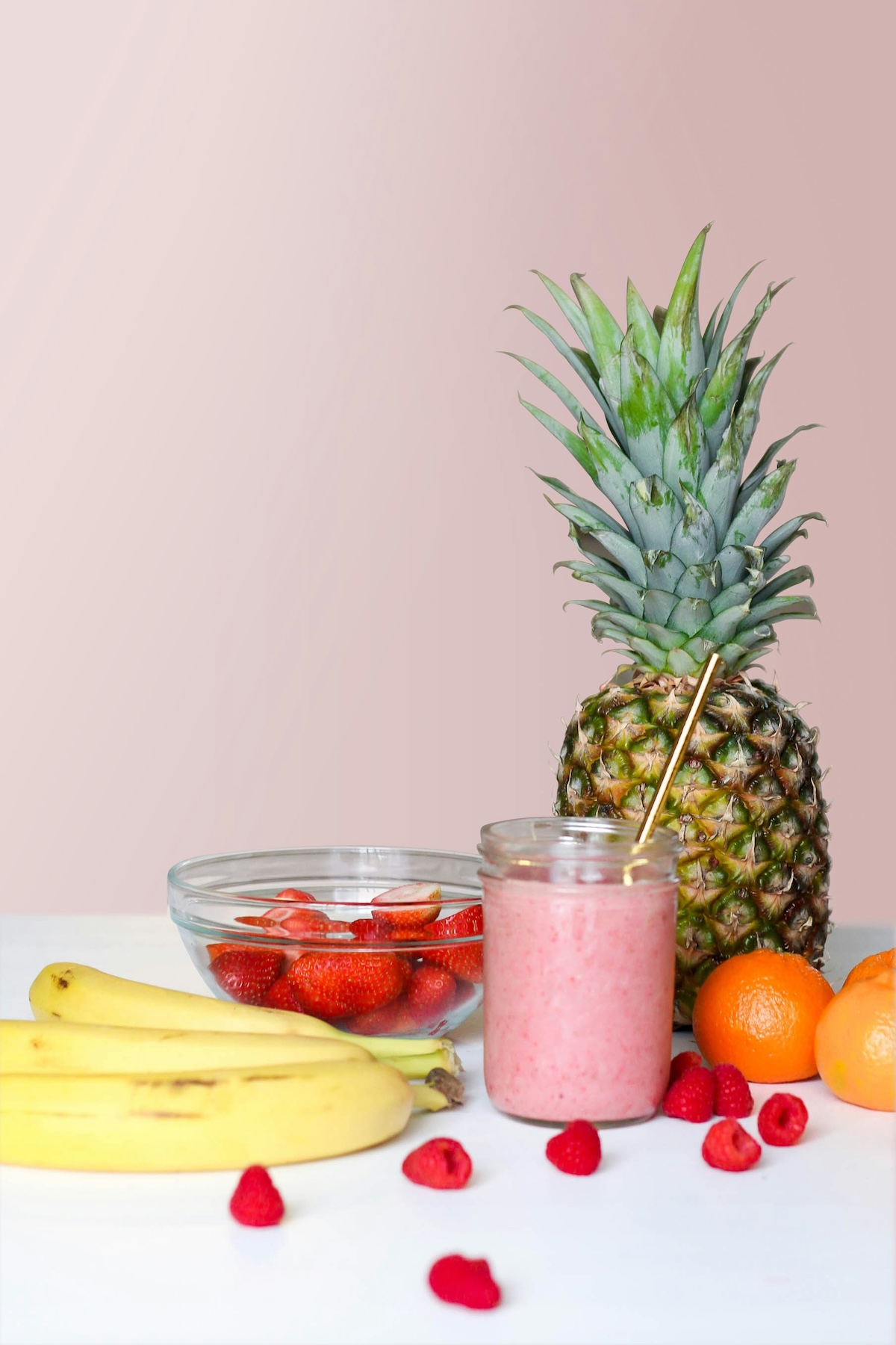 Pink berry smoothie with pineapple, bananas, strawberries and orange ingredients on white table