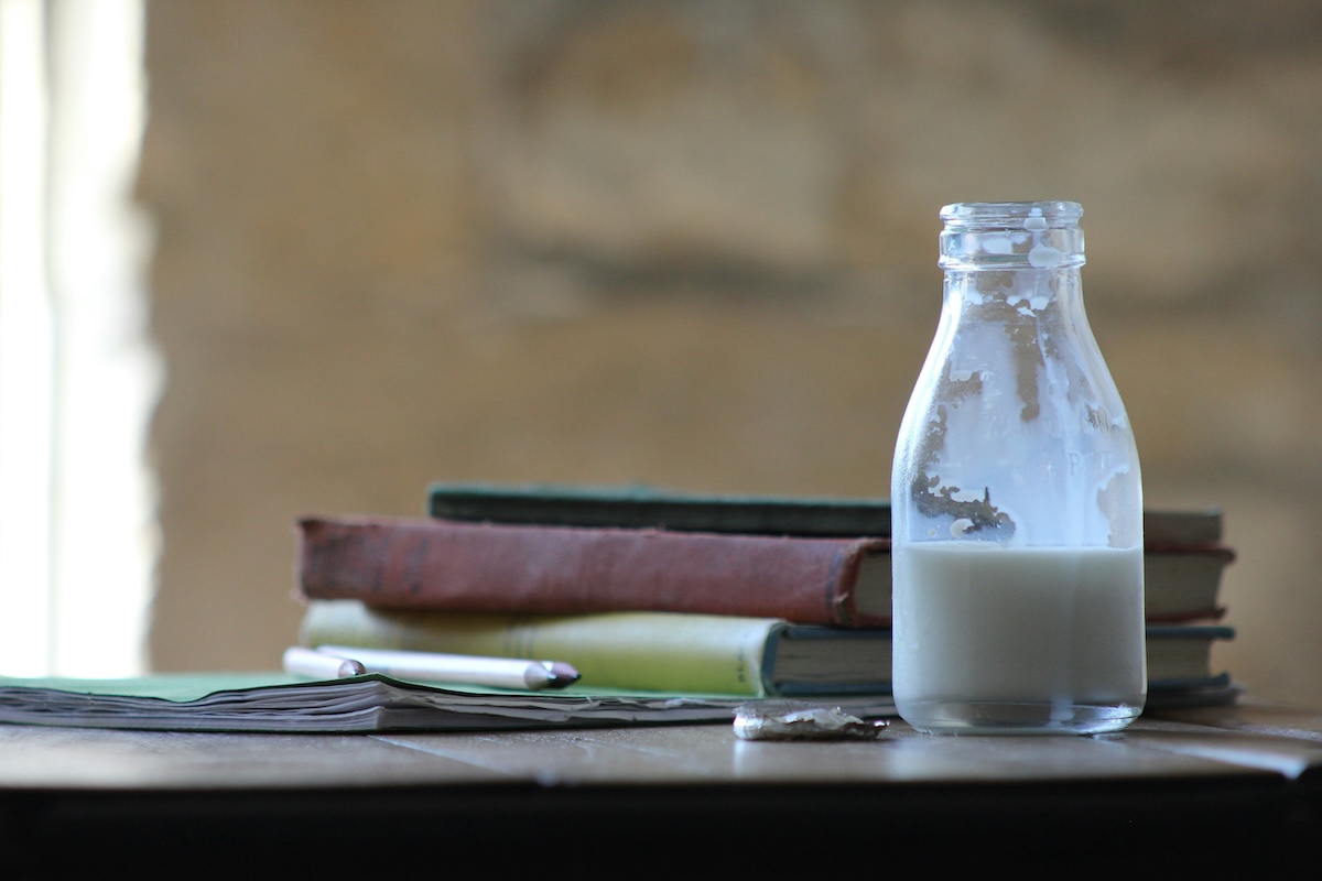 Plant milk bottle with school books and healthy snacks on desk