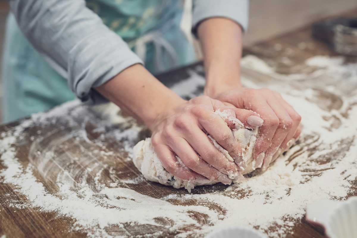 Hands kneading bread dough on floured wooden surface