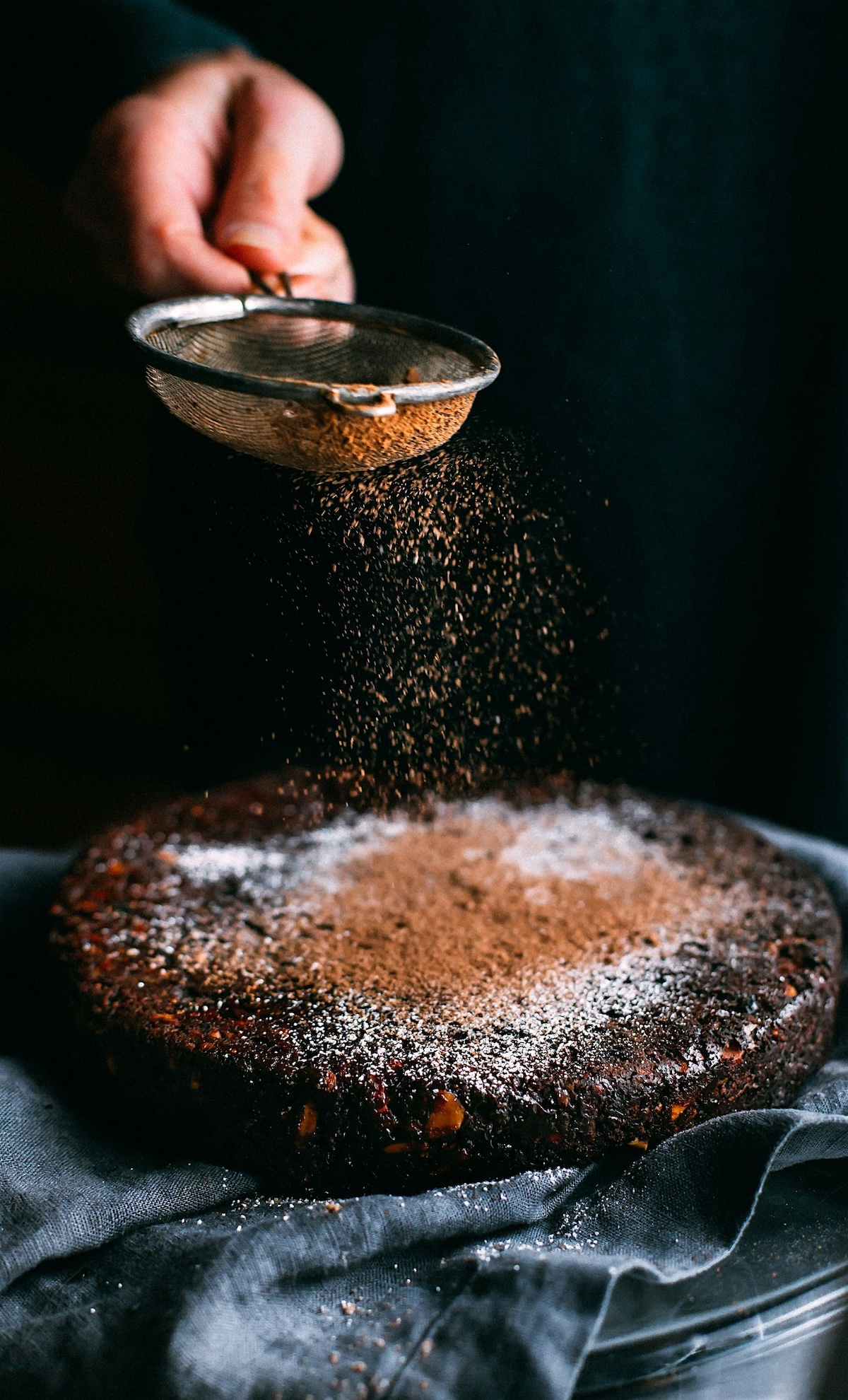 Chocolate cake being dusted with powdered sugar through sieve