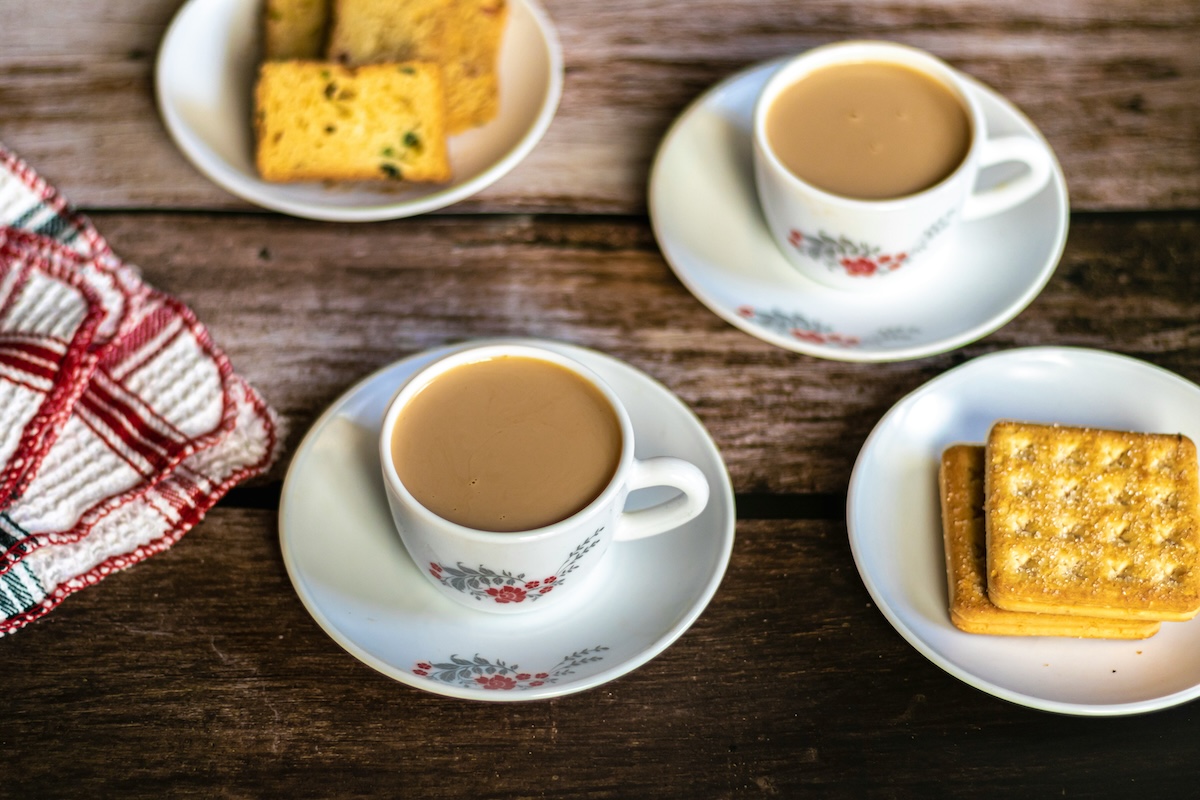 Two cups of tea with plant milk served with biscuits on wooden table
