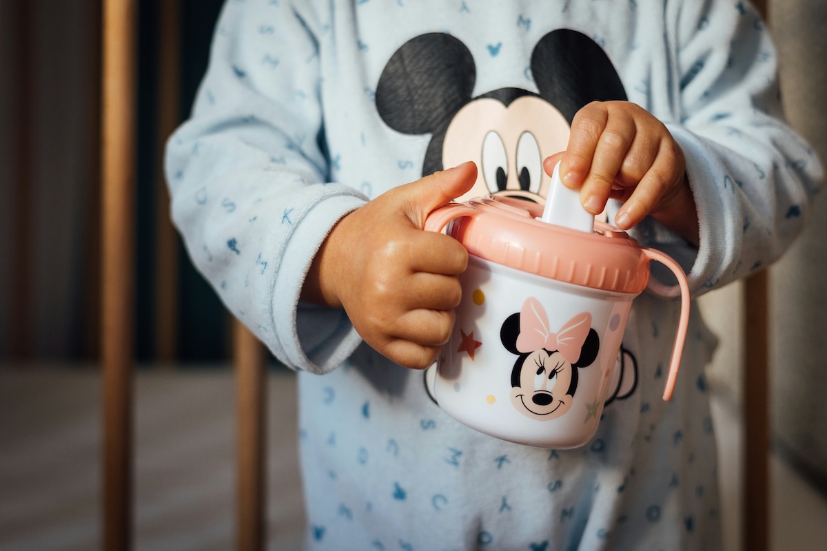 Toddler holding Minnie Mouse sippy cup learning to drink independently