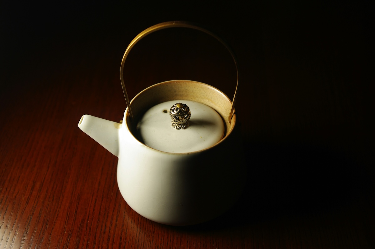 White ceramic teapot with brass handle on wooden table